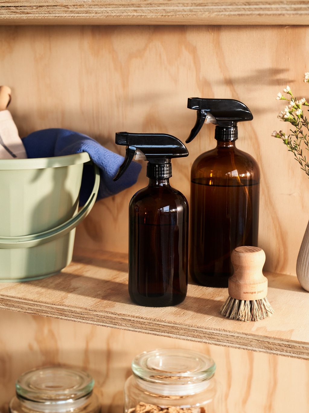 Amber glass spray bottles arranged on a wooden shelf for stylish cleaning storage